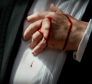 Man wearing a dress shirt, clutching his chest and with blood running down his hand