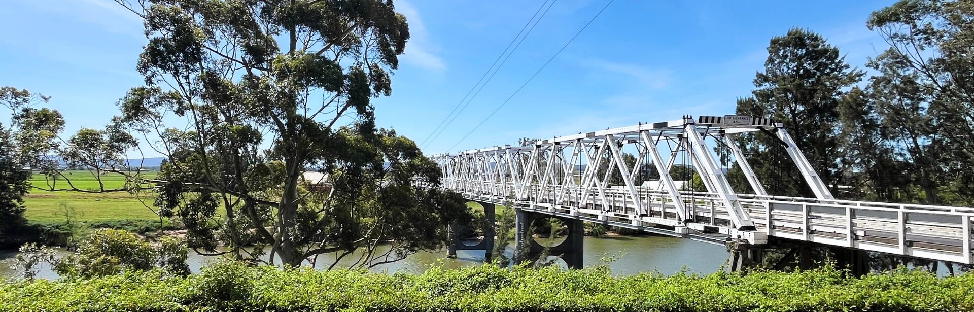 An old white bridge over a river with gum tree lined banks