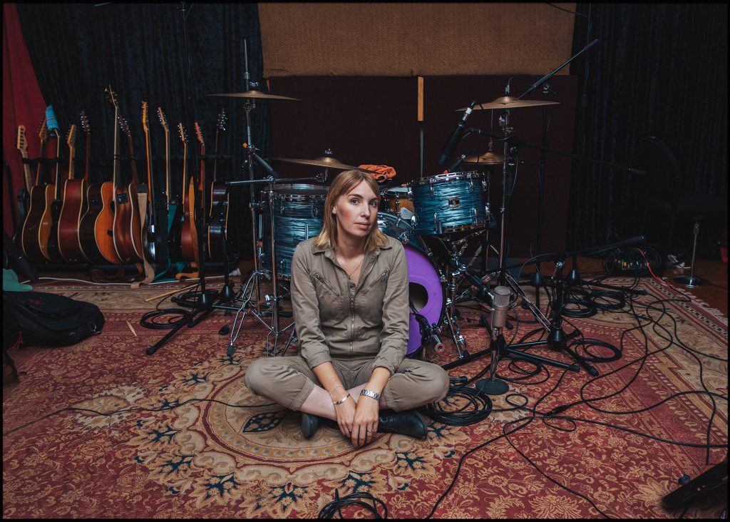 Anna Laverty sits cross-legged on the floor in front of instruments in a music studio.