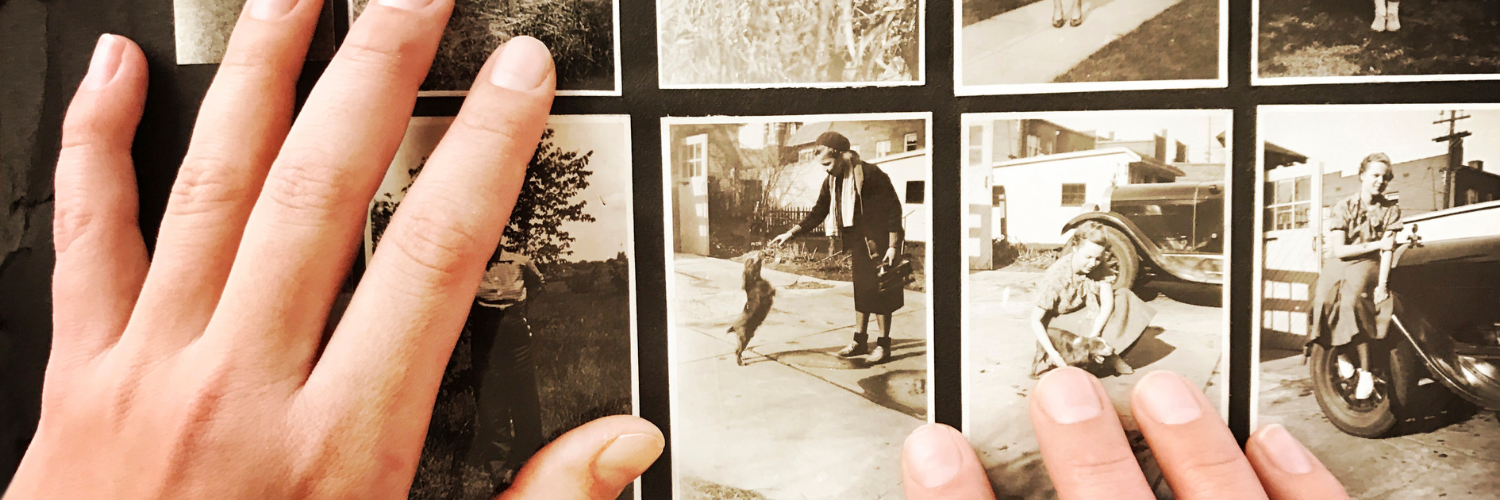 A bird's eye view shows a pair of hands arranging some sepia photos on a black background