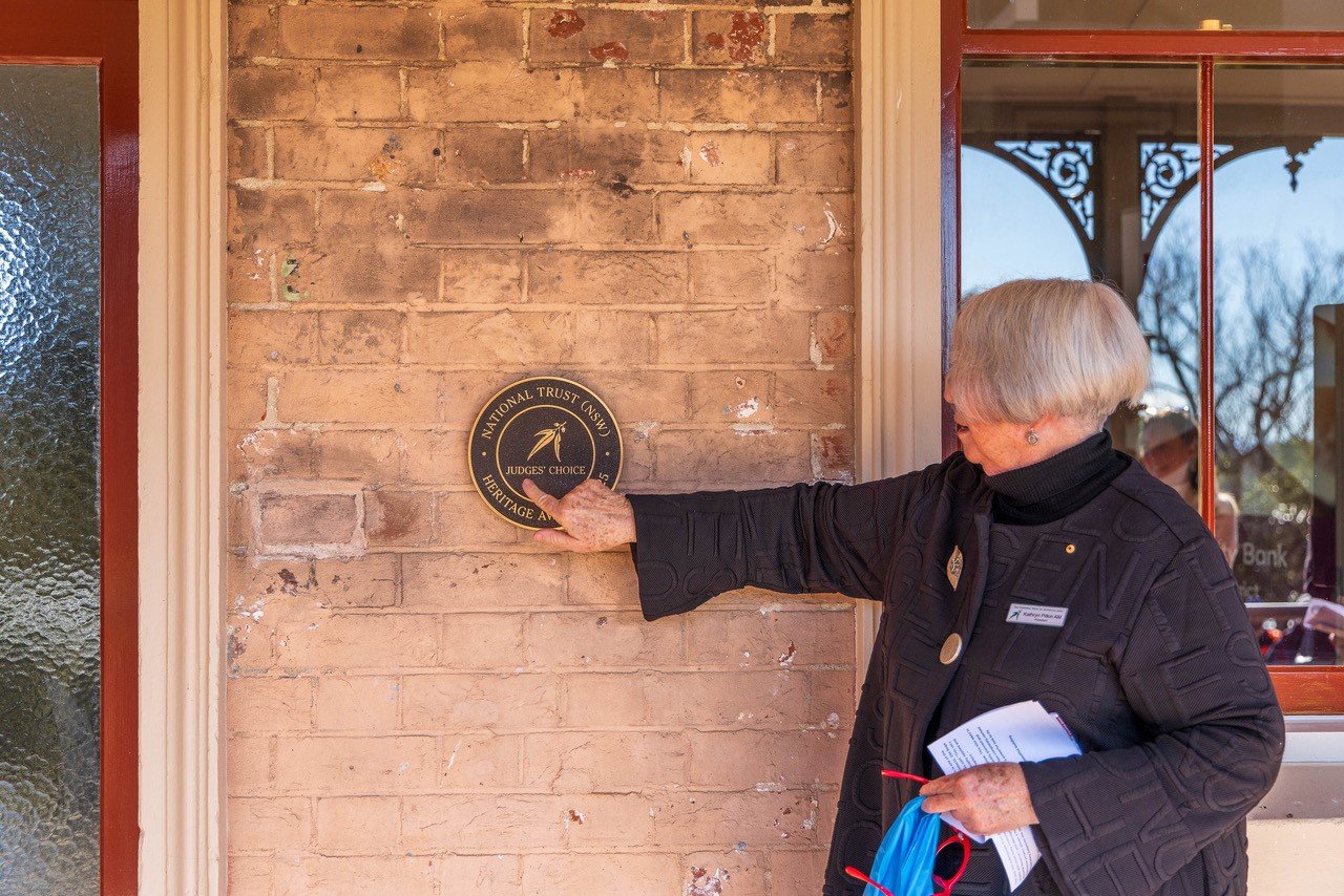A woman points to a plaque on a wall