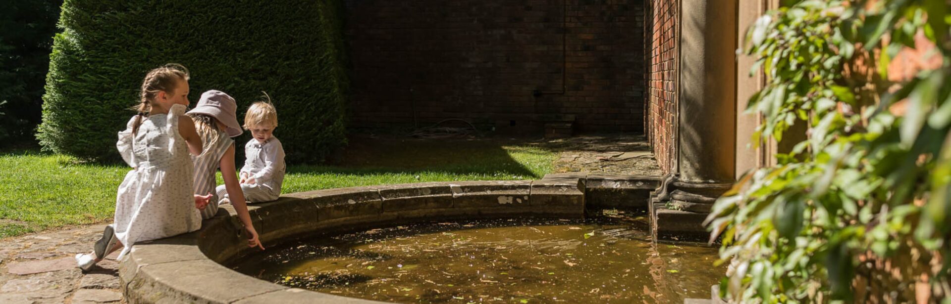 Three children sit next to a round pond