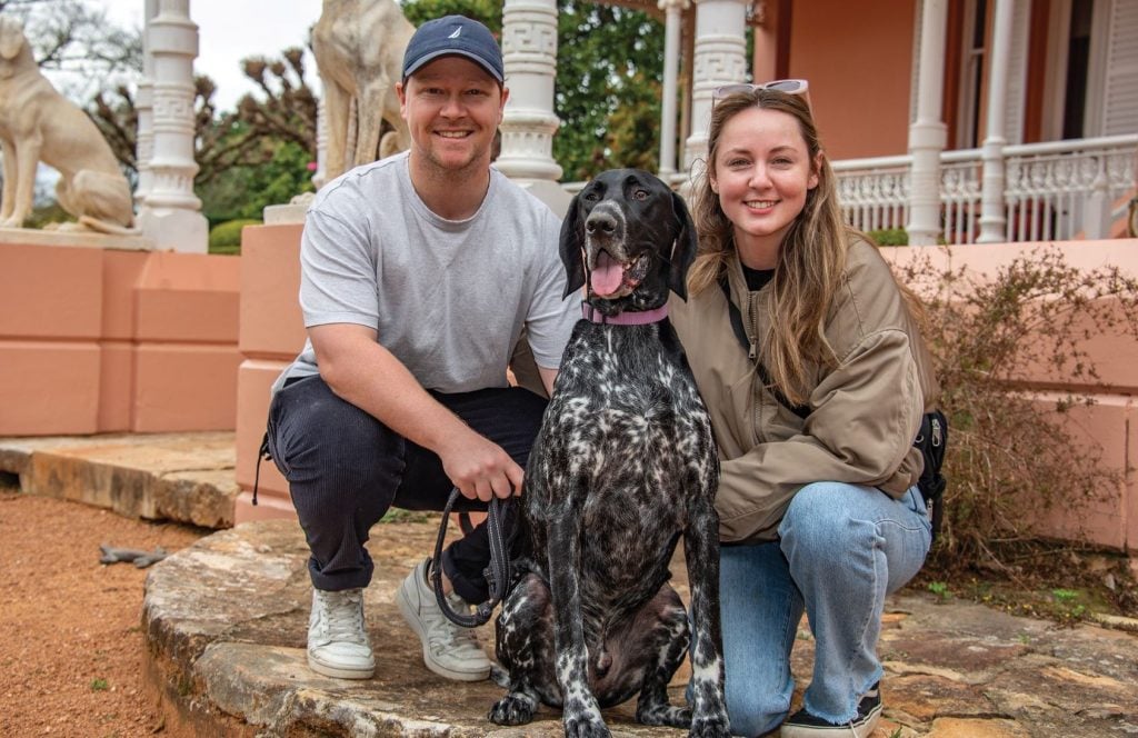 A young man, a young woman and a black and white dog pose for a photo.