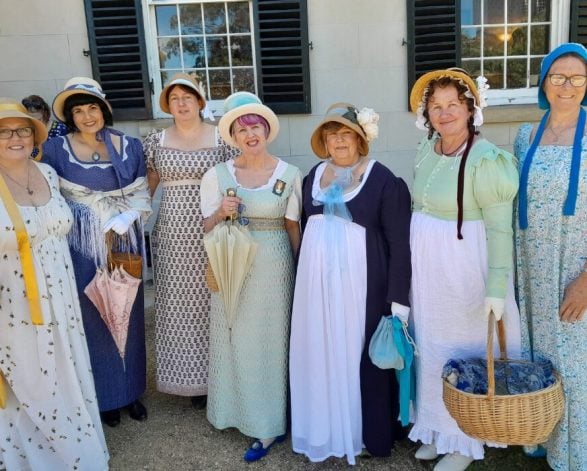 Women dressed in regency attire in front of a heritage building