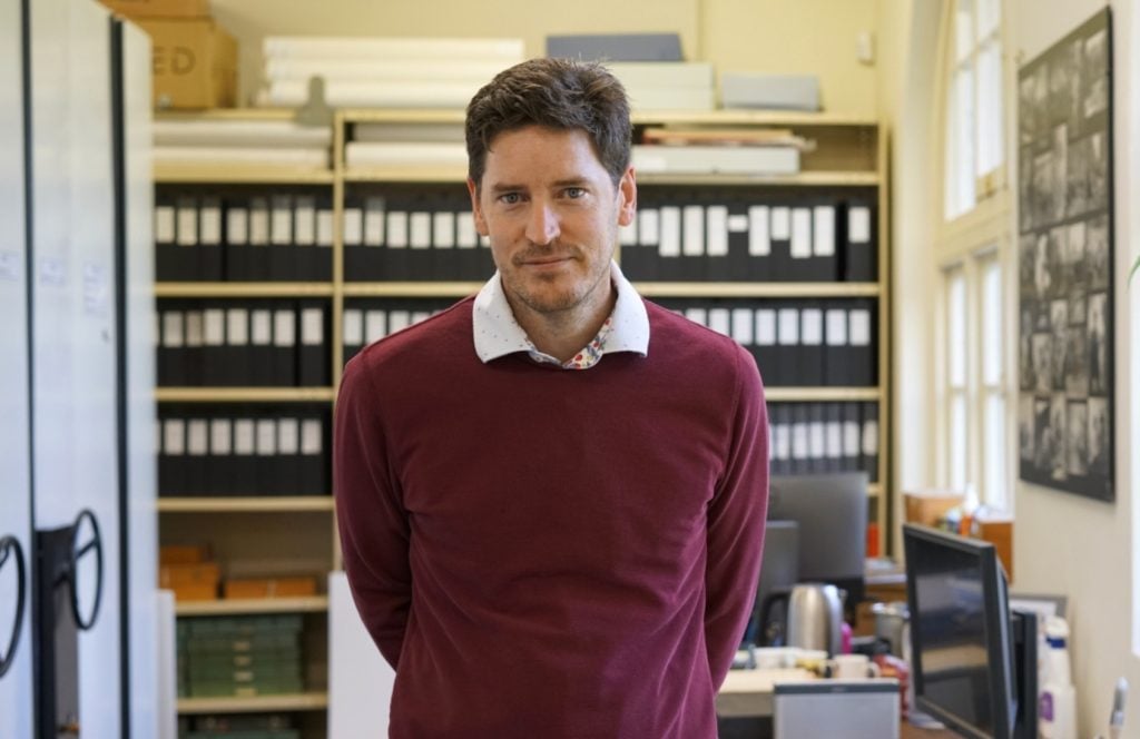 Man with brown hair wearing a burgundy sweater looking at camera.