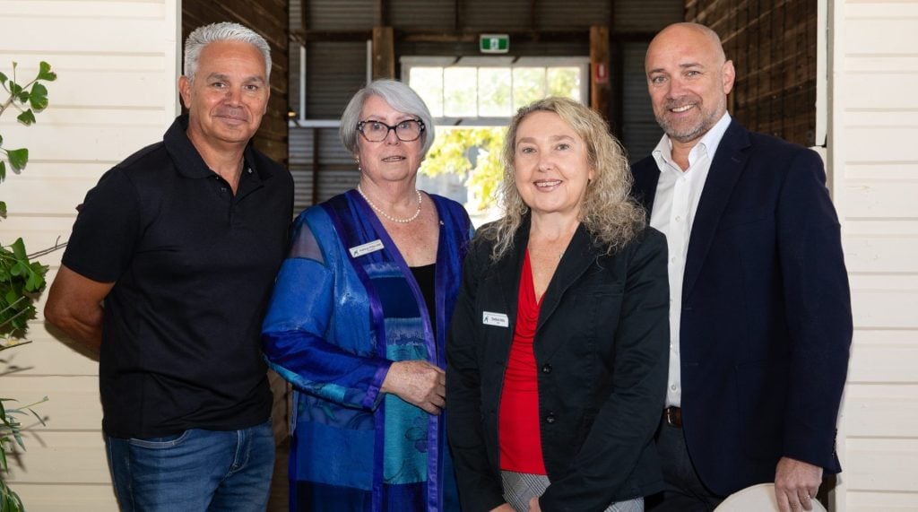 Two men and two women stand outside a farm building smiling at the camera. 
