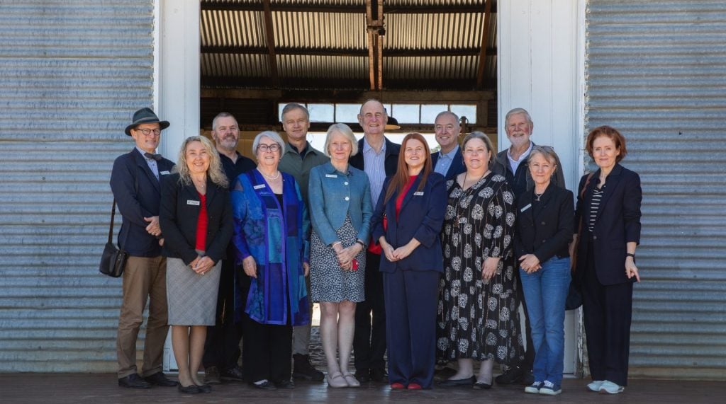 A group of people pose outside a farm building. 