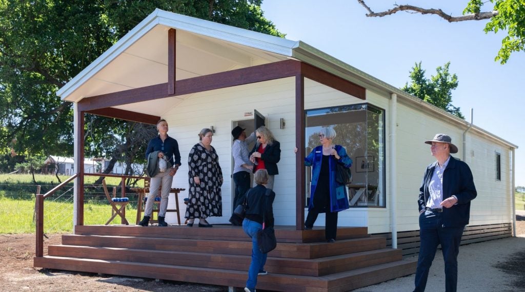 A group of people mingle outside a cabin.