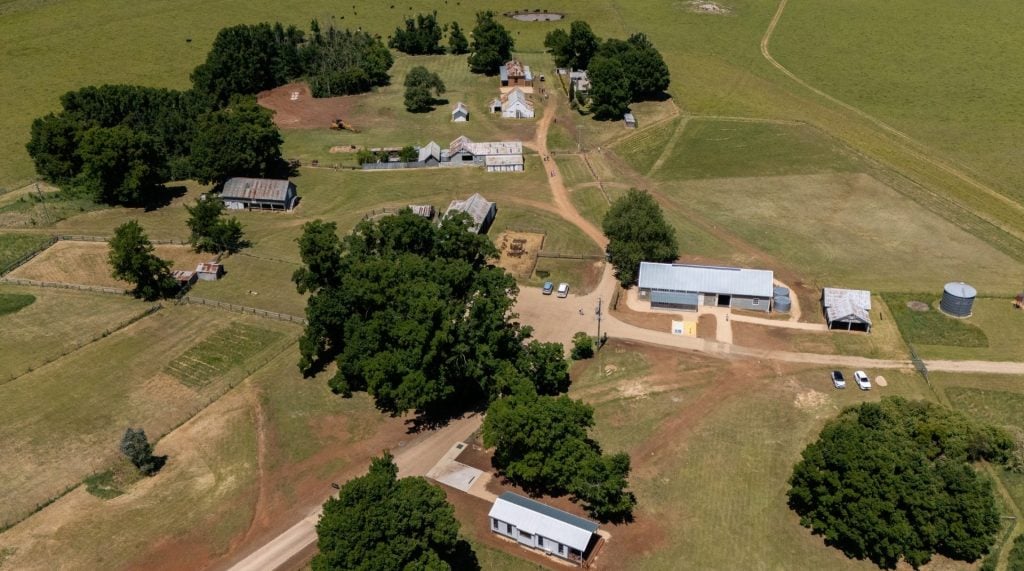 An aerial view depicting farm buildings, fields and trees.