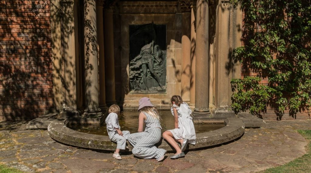 Three children sit on the edge of a shallow pool at Everglades House & Gardens theatre