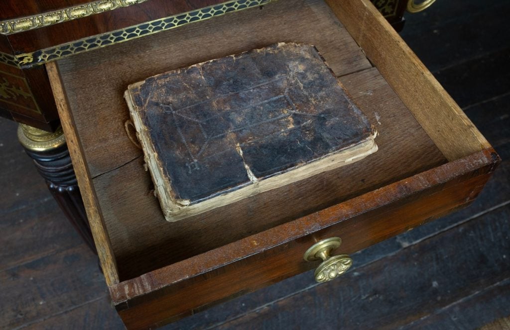 An old bound manuscript inside the wooden drawer of a piano. 
