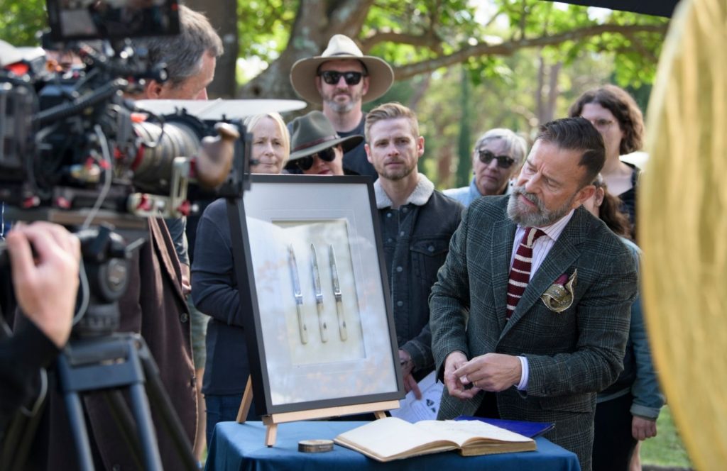 A man in a suit appraises framed knives.
