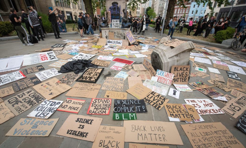 Protest signs surround the site of where a statue once stood.