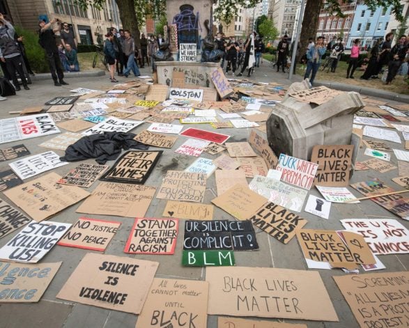 Protest signs surround the site of where a statue once stood